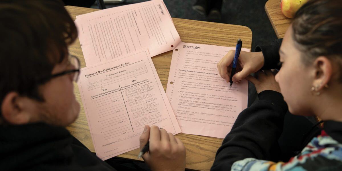 Students leaning over a desk working together on worksheets.