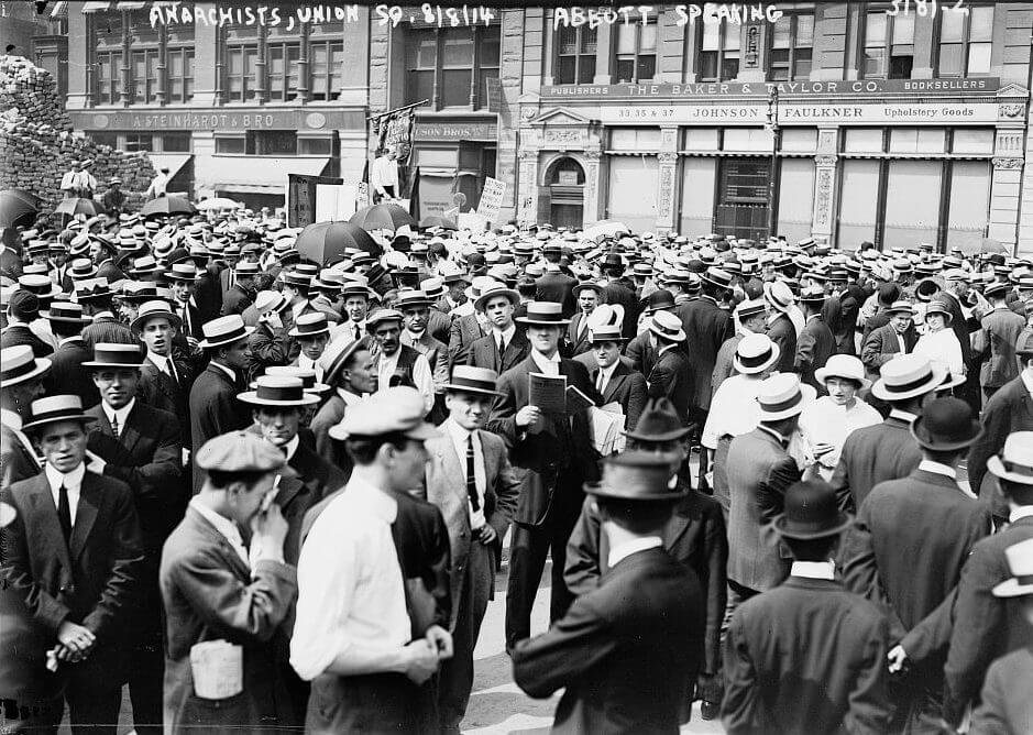 A crowd of men in suits gathered in front of a storefront to protest the war draft.
