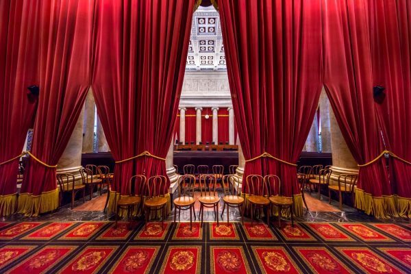Photo of the gallery of the US Supreme Court with red drapery and a line of chairs