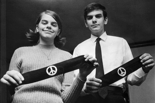 Two Des Moines students holding armbands that symbolized their protest against the Vietnam war. The armbands are black with a white peace sign in the center.